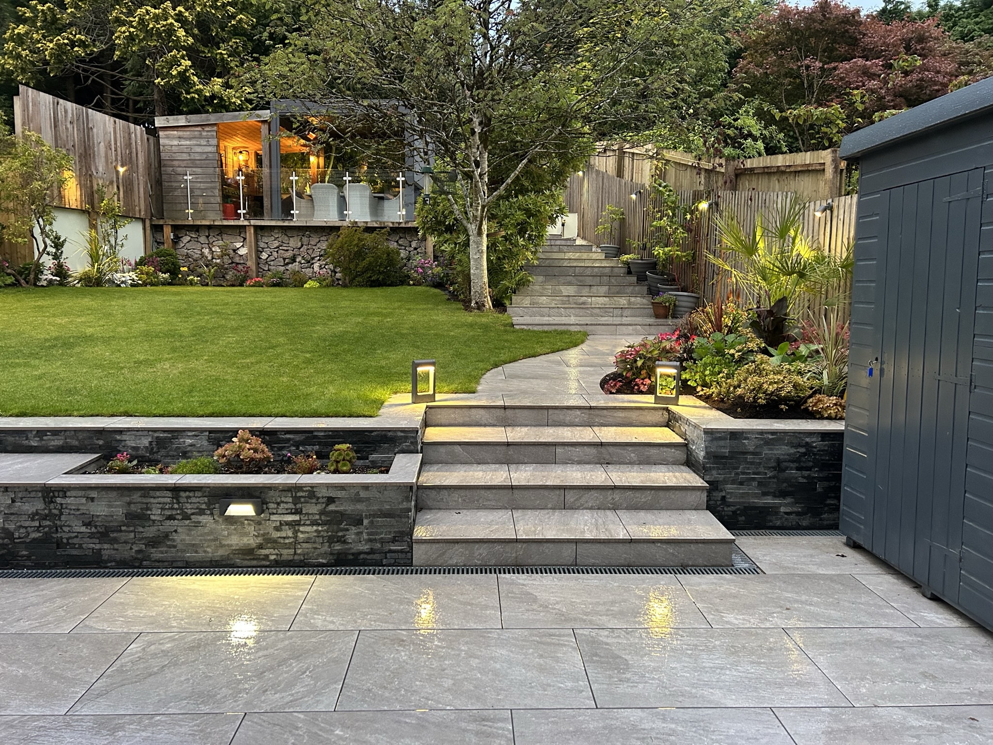 Porcelain patio at dusk with lit steps and a garden room